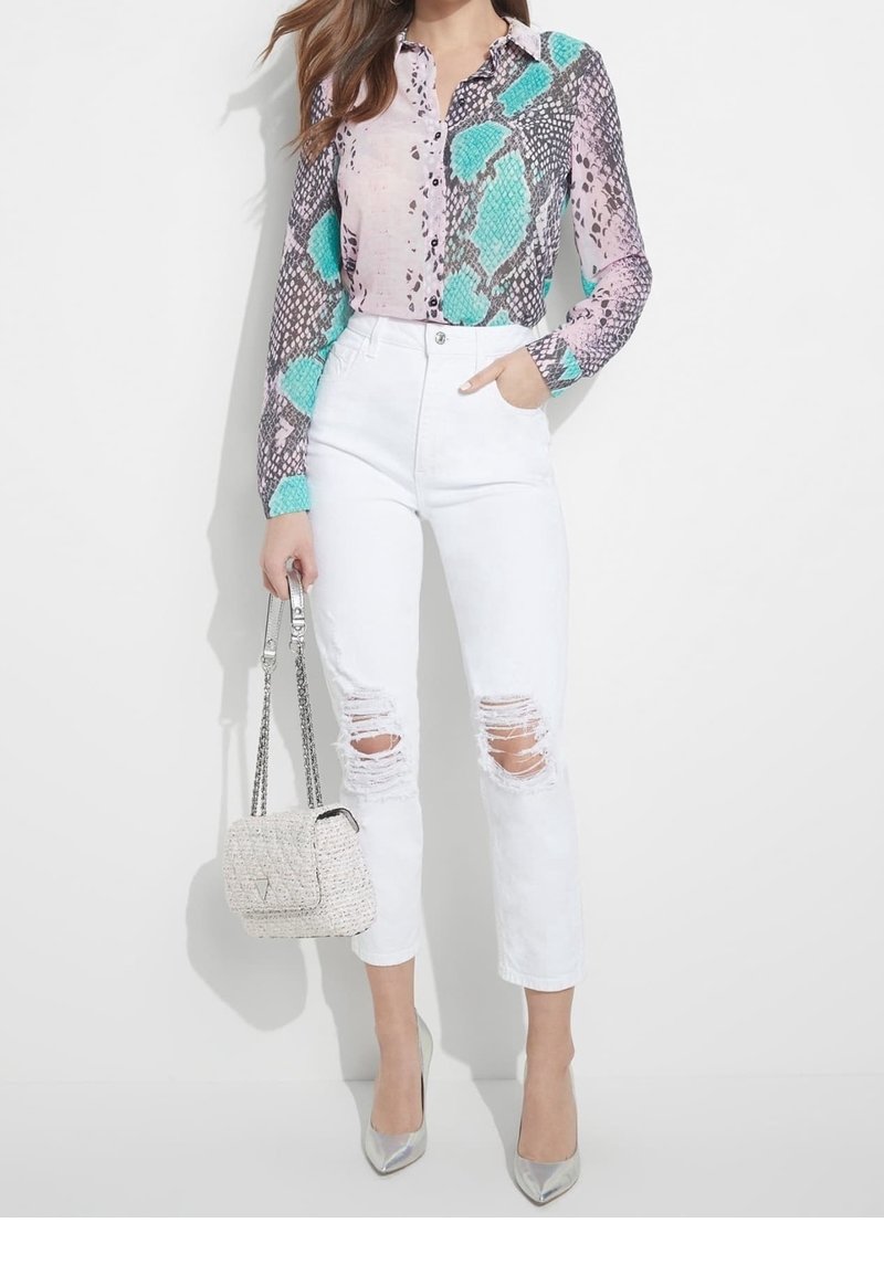 Femme portant un chemisier à manches longues imprimé serpent avec des accents turquoise, un jean blanc déchiré, des talons argentés et tenant un sac à main beige tissé.
