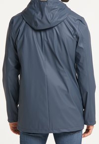 Veste imperméable bleu marine avec capuche, texture lisse, manches longues et coupe droite, présentant des coutures minimales et aucun système de fermeture visible.