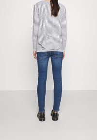 Randig l ångärmad skjorta i vitt och marinblått, ihop med blå skinny jeans och svarta skor, som framhäver en avslappnad, figurnära silhuett.