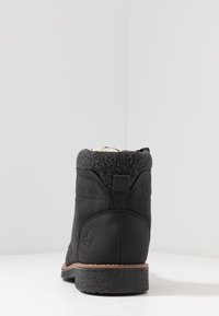 Bottine noire en cuir lisse avec un col en tricot gris. Dispose d'une semelle en caoutchouc plate et d'un détail de logo circulaire sur le côté.