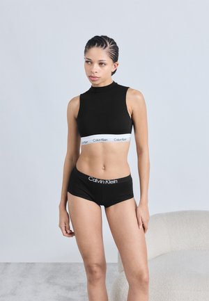 Haut court noir à col haut avec une bande blanche Calvin Klein, associé à un short court noir avec une ceinture blanche portant le logo.