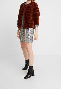 Veste en fausse fourrure marron au design bouffant, portée sur une robe métallisée à imprimé serpent, associée à des bottines noires à talon bloc.