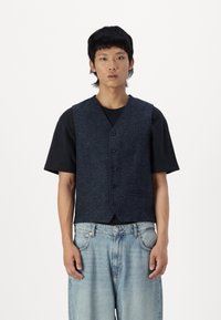 Mørkeblå ullblandingsvest med knappelukking, V-halsdesign og frontlommer, kombinert med en svart t-skjorte og lyse denimjeans.