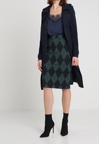 Námornický kabát, modrá tílko s krajkovým okrajem, zelená a černá argyle tužková sukně a černé kotníkové boty na vysokém podpatku.