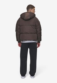 Brun vadderad jacka med huva, med horisontell sömnad, en slät yta och kombinerad med svarta löst sittande jeans och vita sneakers.