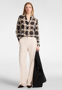 Blusa a maniche lunghe nera e beige con motivo, abbinata a pantaloni larghi crema e un blazer nero. Texture lisce in tutto.