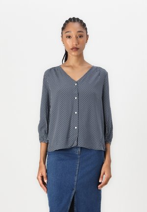 Marineblauwe blouse met een V-hals, knoopsluiting aan de voorkant en driekwartmouwen. Gecombineerd met een denimrok met een split aan de voorkant.