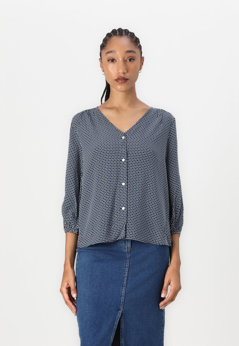 Marineblaue Bluse mit V-Ausschnitt, Knopfverschluss und Dreiviertelärmeln. Kombiniert mit einem Jeansrock mit Schlitz vorne.