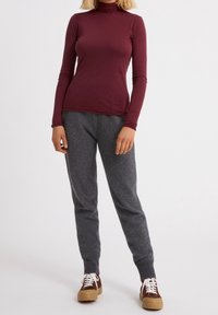 Burgundy pitkähihaisen poolopaidan kanssa yhdistetty harmaat fleece-housut. Housuissa on pehmeä tekstuuri, ja kengät ovat ruskeat valkoisilla nauhoilla.