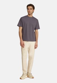 Purple short-sleeve t-shirt, round neckline, paired with light beige trousers and beige sneakers, standing on a plain white background.