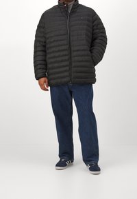 Sort puffet jakke med horisontal quilt og høj krave, parret med løse blå jeans og blå sneakers med hvide striber.