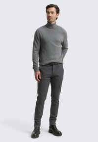 Grijze coltrui gecombineerd met donkergrijze slim-fit broek. Model draagt zwarte enkellaarzen. Glad textuur; geen patronen. Eenvoudig ontwerp.