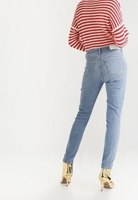 Modré skinny džíny s středním pasem, které mají klasický pětikapsový design, v kombinaci s červeným a bílým pruhovaným svetrem. Zlaté vysoké podpatky dotvářejí vzhled.