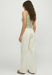 Top sin mangas de punto verde, pantalones anchos blancos y zapatos de lona marrones, sobre un fondo blanco liso. Presenta una tela texturizada y un diseño casual.