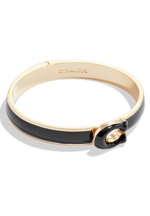 Pulsera brazalete de tono dorado con incrustación de esmalte negro y detalle de cierre en "C" negro, con "COACH" grabado en el interior de la banda.