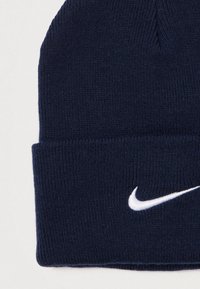 Sötétkék kötött sapka bordázott textúrával és hajtott gallérral, elöl fehér hímzett Nike swoosh logóval.