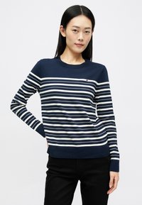 Maglione blu navy con strisce bianche orizzontali, collo a giro e maniche lunghe. Presenta un piccolo logo sul lato sinistro del petto e polsini a coste.
