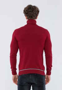 Czerwona sweter z golfem o dopasowanym kroju, z prążkowanym kołnierzem i mankietami oraz kontrastującym białym paskiem u dołu, wykonany z miękkiego materiału dzianinowego.