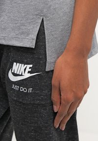 Šedé tričko s krátkým rukávem a bočními rozparky, spárované s černými tepláky. Kalhoty mají bílou ikonu Nike a text "JUST DO IT".