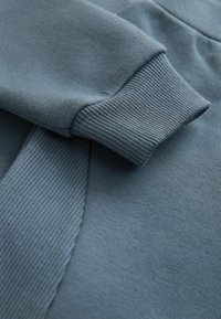 Blaues Baumwoll-Sweatshirt mit gerippten Bündchen und glatter Textur; Nahaufnahme zeigt die Stoff- und Nähdetails.