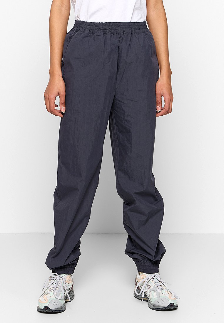 Donkergrijze, lichte, elastische broek met een losse fit en elastische boorden. Gecombineerd met gemusterde sportschoenen.