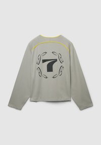 Maglietta a maniche lunghe grigia chiara con bordo giallo sulla parte superiore della schiena e grande numero 7 nero circondato da un design astratto circolare sul retro.