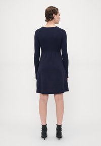 Abito lavorato a maglia blu marina con maniche lunghe, corpetto aderente e gonna svasata. Presenta un collo rotondo e una texture liscia; abbinato a stivaletti neri alla caviglia.