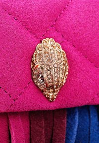 Fuchsia suede purse with diamond-studded shell-shaped clasp, featuring quilted texture and fringed accents.