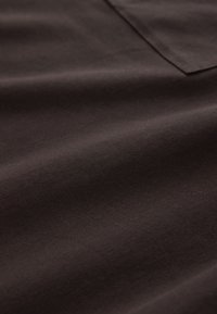 Tissu marron foncé avec une texture lisse et des coutures visibles le long d'une couture et du bord d'une poche.