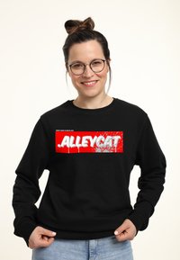 Černá mikina s výraznou červenou grafikou a bílým nápisem "ALLEYCAT", zdůrazňující moderní, městský design.