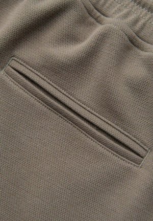 Nahaufnahme eines khakifarbenen, strukturierten Stoffes mit einer horizontalen Schlitztasche und sauberer Steppnaht auf der Kleidungsoberfläche.