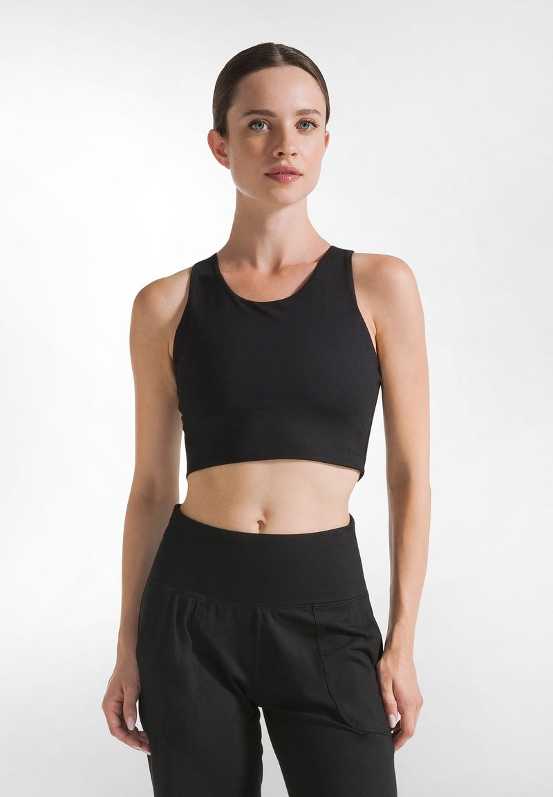 Top deportivo negro con un corte corto, fabricado en tejido suave, con un escote redondo y tirantes anchos, combinado con pantalones negros de cintura alta.