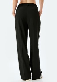 Zwarte wijde broek met een gladde textuur, voorzien van een grijze zijstreep en een achterzak. Eenvoudig ontwerp van de tailleband, zonder zichtbare sluitingen.