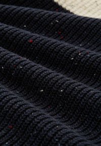 Marineblaues Strickgewebe mit geribbter Textur, das rote und weiße Sprenkel aufweist. Das Material ist dick und weich und zeigt ein gemütliches Design.