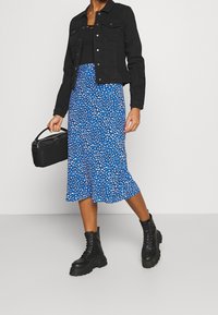 Zwarte denimjack over een zwart top, gecombineerd met een blauw patroonrok en chunky zwarte combat boots, met een kleine zwarte tas.