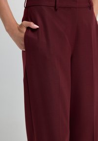 Bordeauxkleurige broek met een op maat gemaakte pasvorm, voorzien van een zijzak en een gladde textuur. De tailleband is vlak zonder zichtbare sluiting.