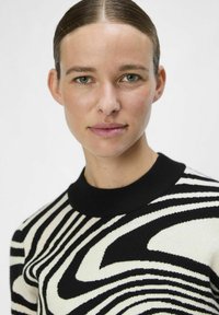 Maglione a righe bianche e nere con un colletto nero a coste. Il tessuto ha una texture liscia, caratterizzato da un motivo ondulato di colori alternati.