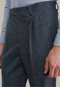 Pantalones azul oscuro con rayas finas claras, hechos de un tejido texturizado, con cierre de botón y bolsillos laterales, con un ajuste entallado.