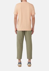 Licht perzikkleurig katoen T-shirt gecombineerd met olijfgroene linnen broek, met een ontspannen pasvorm. Witte sneakers met blauwe accenten maken de look compleet.