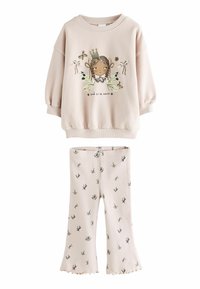 Jasnoróżowy sweatshirt z grafiką dziewczyny i napisem. Pasujące jasnoróżowe spodnie ze żłobionego materiału z zielonymi wzorami liści i poszerzanymi nogawkami.