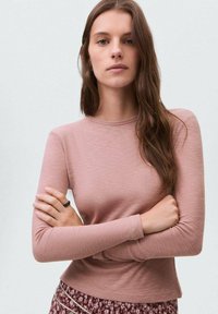 Svetle růžový dlouhý rukáv ribbed top s kulatým výstřihem, který má přiléhavý střih a hladkou texturu, v kombinaci s vzorovanými kalhotami.