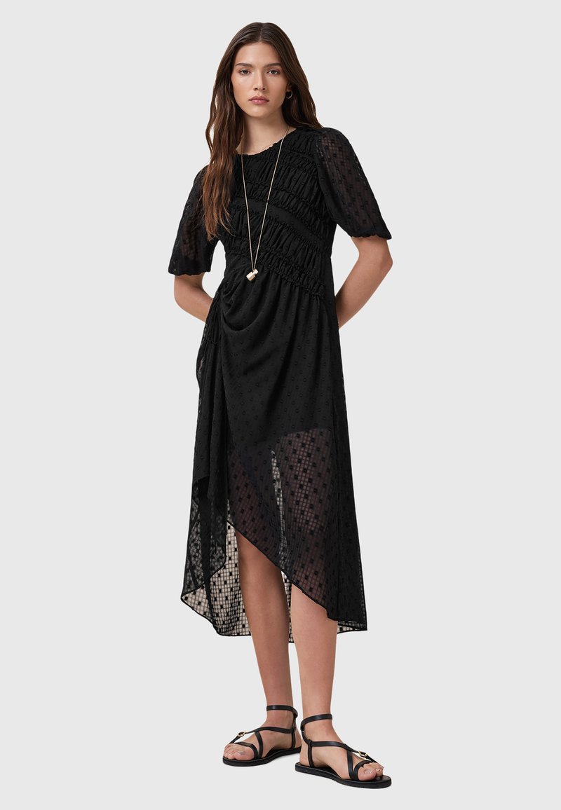 Vestido negro con mangas cortas abullonadas, tejido texturizado, dobladillo asimétrico y detalles fruncidos. Combina con sandalias negras con tiras.