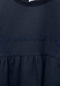 Tummansininen mekko, jossa on teksturoitu neulepäällinen, jossa on vaakasuoria koristeellisia nauhoja ja kerroksittain oleva röyhelö vyötäröllä.