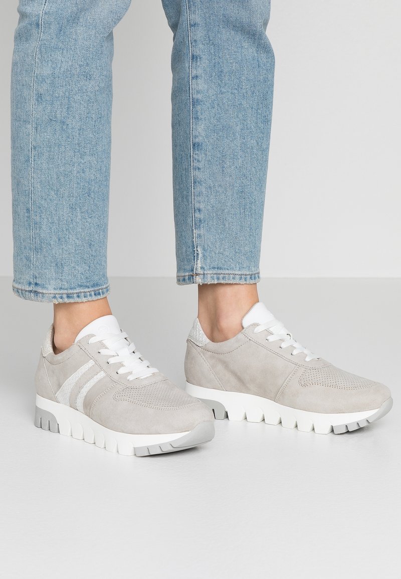 Harmaat mokkanahkaiset tennarit valkoisilla yksityiskohdilla, kuten nauhoilla ja kolmella raidalla. Kenkäpäällä on tekstuuri ja paksu valkoinen kumipohja.