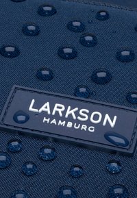 Tessuto blu navy con superficie testurizzata presenta gocce d'acqua e una placca brandizzata che recita "LARKSON HAMBURG" in bianco.