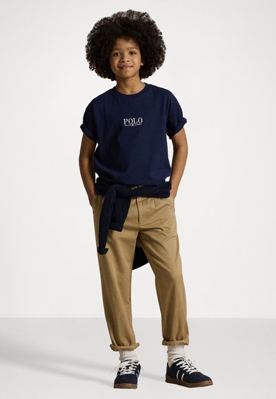 Námornícky bavlnený tričko s otočenými rukávmi obsahuje biely logo "POLO"; skombinované s khaki nohavicami a námorníckymi teniskami s bielymi akcentami a šnúrkami.
