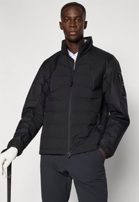 Μαύρο επενδυμένο μπουφάν με φερμουάρ μπροστά, ψηλό γιακά και ελαστικές μανσέτες, με πλαϊνές τσέπες και λογότυπο στο μανίκι.