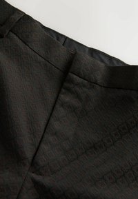 Black fabric trousers with a subtle, dark pattern. Features a smooth texture, side seams, and a waistband silhouette.