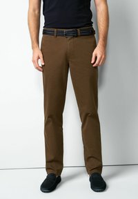 Bruine geruite broek van stof, slim fit, met een zwarte gevlochten riem. Gecombineerd met zwarte instapschoenen.