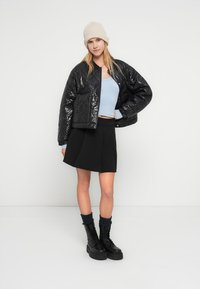 Μαύρο γυαλιστερό μπουφάν puffer με κομμένο σχέδιο, ανοιχτά μπλε τοπ, μαύρη φαρδιά φούστα και μαύρα μποτάκια δένονται με κορδόνια και κάλτσες.